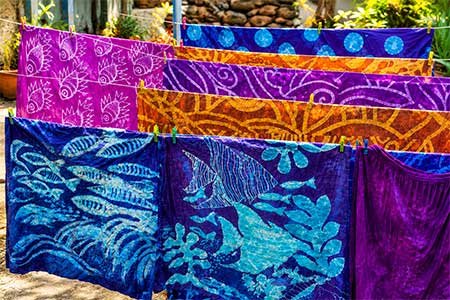 Colourful handmade batik fabrics with tropical patterns hanging outdoors, showcasing Grenadian textile craftsmanship.